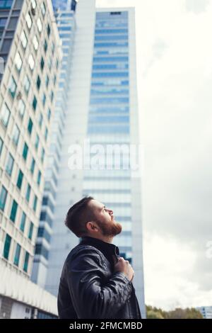 Stilvoller Mann mit Bart vor einem Wolkenkratzer Hintergrund posiert Stockfoto