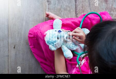 Draufsicht auf einen kinderspielenden Arzt oder eine Krankenschwester mit Plüschtier-Bär zu Hause. Glückliches Mädchen hört ein Stethoskop zu Spielzeug. Verspielte Mädchen Rollenspiel. Stockfoto