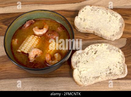 Hausgemachtes, in einer grünen Schüssel serviertes, mit Mais, neuen Kartoffeln und Andouille-Wurst mit zwei Scheiben Sauerteig-Brot zum Kochen bringen Stockfoto