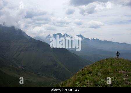 Ein einsamer Wanderer, der über ein Tal in den Drakensberg-Bergen Südafrikas blickt, mit den hohen Gipfeln, die von den sich aufziehenden Wolken verborgen sind. Stockfoto