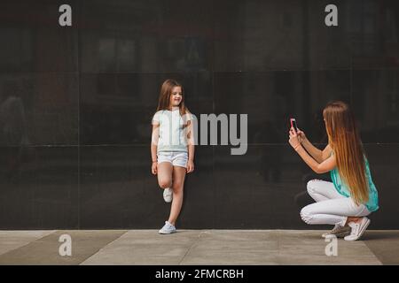 Glückliche Mutter, portrait Kind auf dem Smartphone in der Stadt, der Familie das Tragen eines T-Shirts und Weiße Shorts Stockfoto