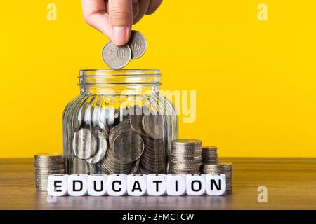 Viele Münzen im Glas-Geldbecher mit gelbem Hintergrund. Sparkonzept für Bildung. Stockfoto