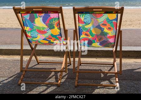 Zwei farbenfrohe Liegestühle, Liegestühle, fruchtiges Musterdesign an der Promenade in Bournemouth, Dorset UK im Mai - Liegestuhl mit Blick auf das Meer Stockfoto