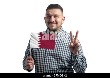 Weißer Kerl hält eine Flagge von Katar und zeigt zwei Finger isoliert auf einem weißen Hintergrund. Stockfoto