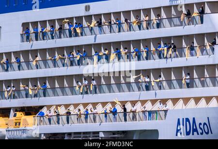 Rostock, Deutschland. Mai 2021. Die Crew-Mitglieder winken Badetücher von den Balkonen des Kreuzfahrtschiffs „AIDAsol“, wenn es in den Hafen einfährt. Das Schiff kommt anlässlich der Nationalen Seeverkehrskonferenz am 10.05.2021 und der Einweihung des neuen Landkraftwerks nach Warnemünde. Quelle: Jens Büttner/dpa-Zentralbild/dpa/Alamy Live News Stockfoto