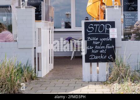 Pelzerhaken, Deutschland. Mai 2021. Auf einem Schild vor einem Restaurant steht: „Stop - Please wait here! Wir holen Sie hier ab! Vielen Dank!“ Ablesbar. Unter strengen Auflagen haben Hotels, Campingplätze und Restaurants an der Lübecker Bucht wieder geöffnet. Insgesamt beteiligen sich nach Angaben des Distrikts rund 300 Unternehmen an dem Pilotprojekt. Quelle: Frank Molter/dpa/Alamy Live News Stockfoto