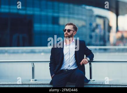 Auf dem Hintergrund sitzt ein junger erfolgreicher Geschäftsmann im Anzug Eines Bürogebäudes Stockfoto