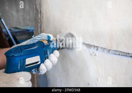 Ein Arbeiter bohrt ein Loch für eine Steckdose in eine Betonsteinwand. Reparatur der elektrischen Verkabelung. Bauarbeiter Mann mit pneumatischem Hammer dr Stockfoto