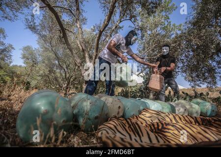 08. Mai 2021, Palästinensische Gebiete, Juhor ad-Dik: Maskierte Anhänger der Bewegung des Islamischen Dschihad in Palästina bereiten sich darauf vor, Ballons mit Kältemittelgas zu füllen und an Brandvorrichtungen und brennbares Material zu befestigen, bevor sie von Wind auf israelisches Gebiet in der Nähe des Dorfes Juhor ad-Dik, das östlich von Gaza-Stadt liegt, freigesetzt werden. Mehr als 200 Menschen wurden bei schweren Zusammenstößen zwischen Palästinensern und israelischen Sicherheitskräften in der Altstadt von Jerusalem auf dem heiligen Ort, der den Juden als Tempelberg und den Muslimen als Edles Heiligtum oder Al Aqsa Compo bekannt ist, verletzt Stockfoto