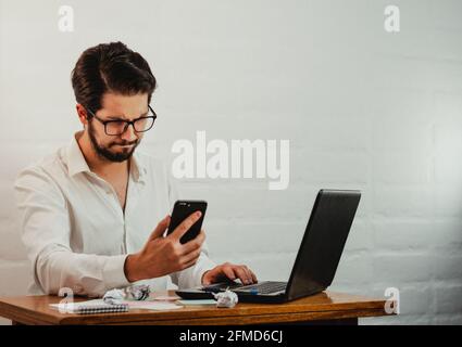Junge kaukasische männliche Blick auf das Telefon mit ernster Gesichtsbehandlung Ausdruck während der Arbeit im Büro Stockfoto