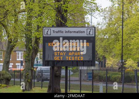 Auf dem elektronischen Schild am Straßenrand in Southend-on-Sea wird die COVID-19-Meldung „WEITER GEHEN SOS / SICHER BLEIBEN / GETRENNT BLEIBEN / GETESTET WERDEN“ zwischen Bäumen und Häusern angezeigt. Stockfoto