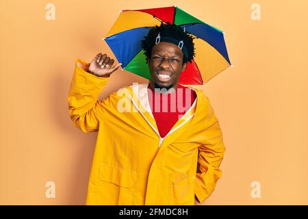 Junger afroamerikanischer Mann mit gelbem Regenmantel, der sich zurückstreckt, müde und entspannt, müde und gähnend für den frühen Morgen Stockfoto