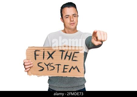 Hübscher junger Mann, der die Systembanner-Pappe hält und mit dem Finger auf die Kamera und auf Sie zeigt, selbstbewusste Geste, die ernst aussieht Stockfoto