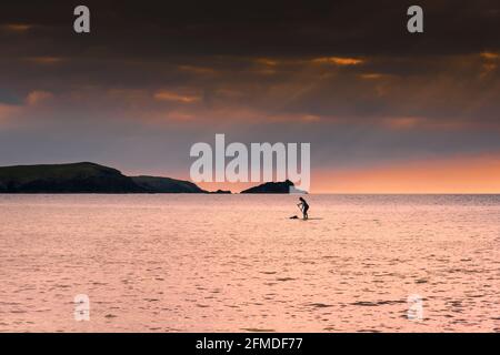 Eine weibliche Stand Up Paddlebarderin paddelt während eines goldenen Sonnenuntergangs in der Fistral Bay in Newquay in Cornwall. Stockfoto