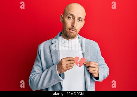 Glatze Mann mit Bart hält gebrochene Herz Papier Form entspannt mit ernsten Ausdruck auf dem Gesicht. Einfach und natürlich Blick auf die Kamera. Stockfoto