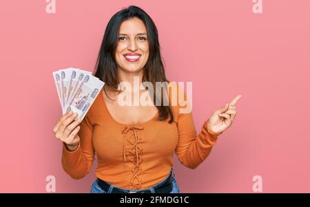 Schöne hispanische Frau hält russische 500 Rubel Banknoten lächelnd glücklich Zeigt mit Hand und Finger zur Seite Stockfoto