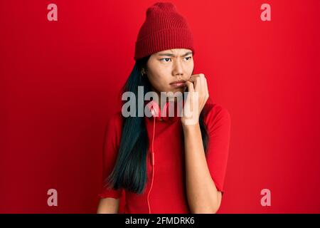 Junge chinesische Frau, die Musik mit Kopfhörern hören, die gestresst und nervös mit den Händen auf dem Mund aussehen, beißende Nägel. Angstproblem. Stockfoto