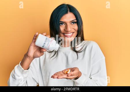 Junge lateinische transsexuelle Transgender-Frau hält Pillen lächelnd zur Seite schauend und starrt weg denkend. Stockfoto