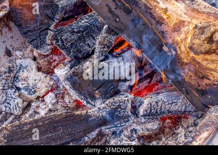 Nahaufnahme einer roten Feuerflamme auf einem brennenden Brennholzbaum. Warmer Winterabend in der Nähe des Kamins, Kochen am Feuer. Stockfoto