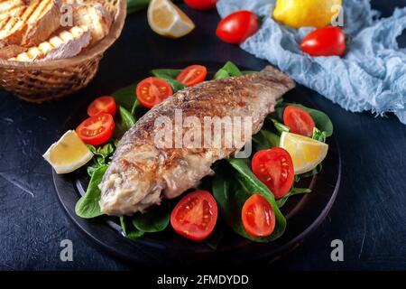 Gegrillter Fisch mit Tomaten, Spinat auf einem Holzbrett. Köstliches und leichtes Abendessen Stockfoto