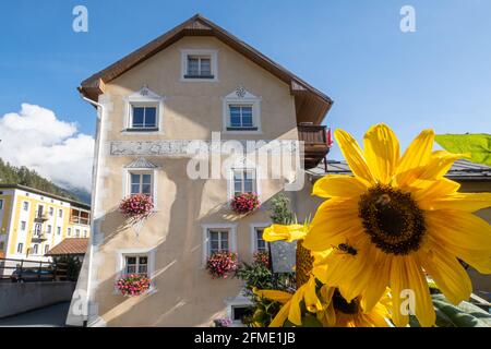 Mustair, Schweiz - 8. September 2020: Sonnenblume und traditionelles altes Haus des Engadins Stockfoto