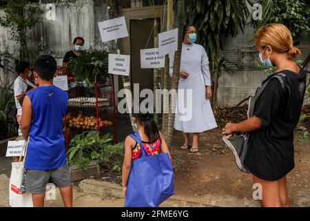 Nonnen halten wach, während Bewohner Schlange stehen, um kostenlose Waren aus einer gemeinschaftlichen Quarantäne zu sammeln, die von den Missionsschwestern des Sacro Costato und der schmerzhaften Mutter (MSC) in Quezon City angeboten wird. Kirchliche Gruppen haben ihre Unterstützung für die wachsende Zahl von gemeindengeführten Vorratskammern bekundet, die Menschen, die von der COVID-19-Pandemie betroffen sind, kostenlose Nahrung zur Verfügung stellen, trotz Anschuldigungen von Gesetzeshütern wie kommunistischen Rebellen oder Unterstützern des langjährigen linken Aufstands im Land. Metro Manila, Philippinen. Stockfoto