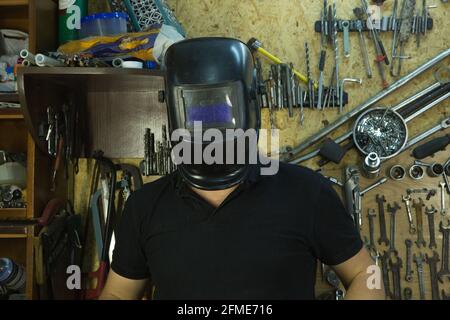 Porträt eines jungen Mannes in der Werkstatt. Der Mann trägt eine Schweißermaske. Stockfoto