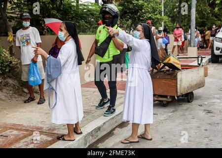 Nonnen halten wach, während Bewohner Schlange stehen, um kostenlose Waren aus einer gemeinschaftlichen Quarantäne zu sammeln, die von den Missionsschwestern des Sacro Costato und der schmerzhaften Mutter (MSC) in Quezon City angeboten wird. Kirchliche Gruppen haben ihre Unterstützung für die wachsende Zahl von gemeindengeführten Vorratskammern bekundet, die Menschen, die von der COVID-19-Pandemie betroffen sind, kostenlose Nahrung zur Verfügung stellen, trotz Anschuldigungen von Gesetzeshütern wie kommunistischen Rebellen oder Unterstützern des langjährigen linken Aufstands im Land. Metro Manila, Philippinen. Stockfoto