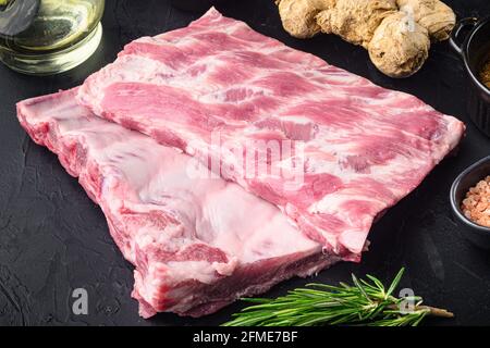 Frisches Rack aus rohen Schweinefleisch Spare Ribs gewürzt mit Gewürzen Set, auf schwarzem Stein Hintergrund Stockfoto