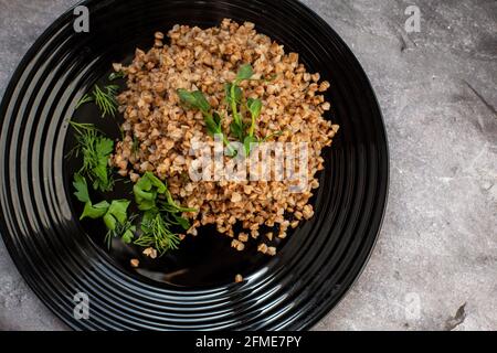 Der gekochte Buchweizenbrei mit den Kräutern und den Sprossen der Erbsen auf dem schwarzen Teller. Stockfoto