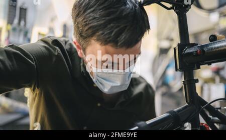 Fahrradwerkstatt arbeitet in der Fahrradwerkstatt während der Coronavirus-Quarantäne mit Gesichtsschutz und Handschuhen, neue Norm. Mechaniker Stockfoto