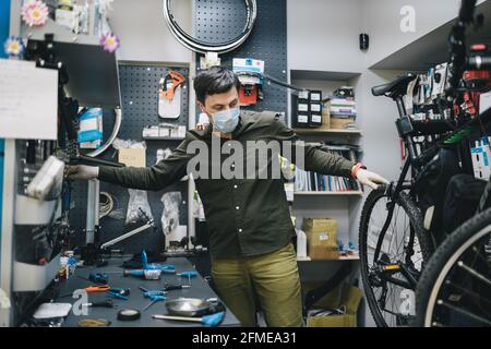 Fahrradwerkstatt arbeitet in der Fahrradwerkstatt während der Coronavirus-Quarantäne mit Gesichtsschutz und Handschuhen, neue Norm. Mechaniker Stockfoto
