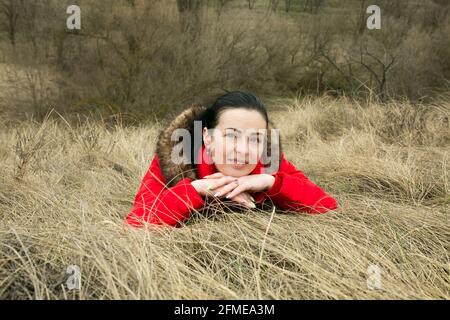 Dnepropetrovsk, Ukraine - 04.08.2021 - EINE schöne schwarzhaarige Frau liegt im Frühjahr auf dem gelben Gras. Die Frau genießt die Frühlingssonne und geht Stockfoto