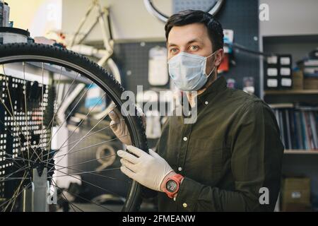 Fahrradwerkstatt arbeitet in der Fahrradwerkstatt während der Coronavirus-Quarantäne mit Gesichtsschutz und Handschuhen, neue Norm. Mechaniker Stockfoto