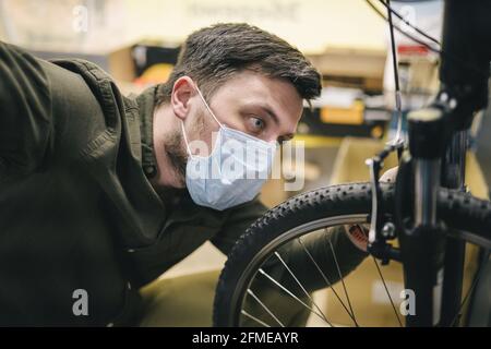 Fahrradwerkstatt arbeitet in der Fahrradwerkstatt während der Coronavirus-Quarantäne mit Gesichtsschutz und Handschuhen, neue Norm. Mechaniker Stockfoto