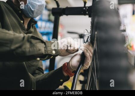 Fahrradwerkstatt arbeitet in der Fahrradwerkstatt während der Coronavirus-Quarantäne mit Gesichtsschutz und Handschuhen, neue Norm. Mechaniker Stockfoto