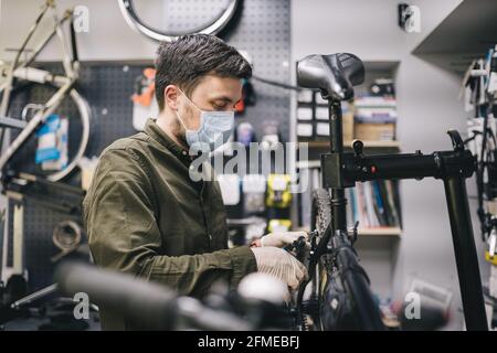 Fahrradwerkstatt arbeitet in der Fahrradwerkstatt während der Coronavirus-Quarantäne mit Gesichtsschutz und Handschuhen, neue Norm. Mechaniker Stockfoto