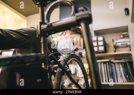 Fahrradwerkstatt arbeitet in der Fahrradwerkstatt während der Coronavirus-Quarantäne mit Gesichtsschutz und Handschuhen, neue Norm. Mechaniker Stockfoto