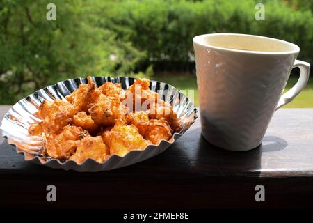 Schmackhafter Reis Bhajiya oder Pakoda auch als Reisbällchen bekannt ist, wird aus übrig gebliebenem Reis, Gramm Mehl in Teller mit heißer Tasse indischer Masala t serviert Stockfoto