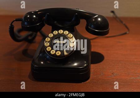 Ein altes schwarzes Drehknopf-Wähltelefon sitzt auf Eine Holztheke Stockfoto