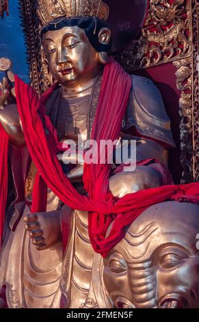 Fengdu, China - 8. Mai 2010: Geisterstadt, historisches Heiligtum. Nahaufnahme eines ernsthaften goldenen Buddha, der auf einem Elefanten mit rotem Schal sitzt. Stockfoto