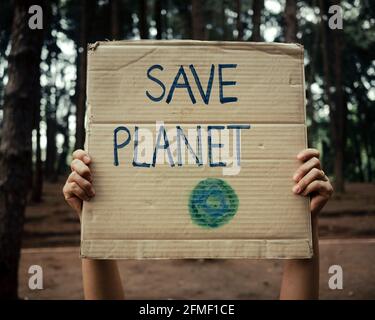 Hand hält Banner, die gegen Verschmutzung und globale Erwärmung im Wald protestieren, um den Planeten Erde zu retten. Das Konzept des Weltumwelttages. Stockfoto