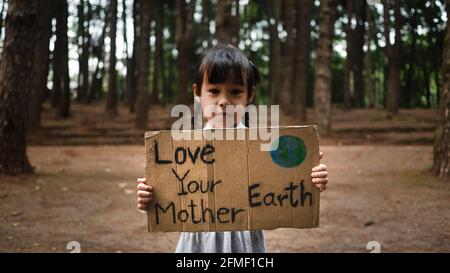 Das kleine Mädchen mit Transparenten, die gegen Umweltverschmutzung und globale Erwärmung im Wald protestieren, um den Planeten Erde zu retten. Das Konzept der Weltumwelt D Stockfoto