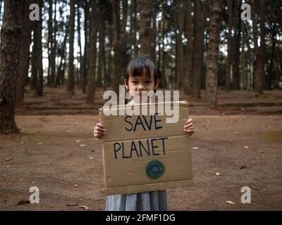 Das kleine Mädchen mit Transparenten, die gegen Umweltverschmutzung und globale Erwärmung im Wald protestieren, um den Planeten Erde zu retten. Das Konzept der Weltumwelt D Stockfoto