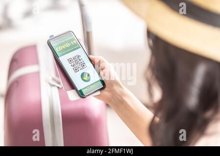 Digitales grünes Zertifikat für internationale Reisen zeigt grüne Covid-19 geimpfte Zecken und einen QR-Code im Smartphone einer Frau. Stockfoto
