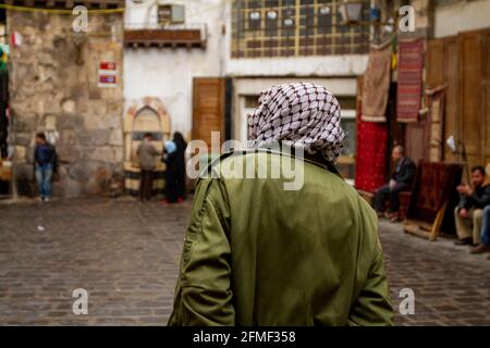 Blick auf die Straße, Innenstadt von Damaskus, Syrien, mit einem Mann von hinten, der in der Altstadt von Damaskus, Syrien, einen Keffiyeh im palästinensischen Stil trägt. Kopfsteinpflaster Stockfoto