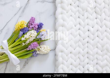 Bouquet von frühlingshaften Blüten von Hyazinthen. Weißer Marmorhintergrund und flauschiges Strickmuster Stockfoto