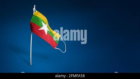 Myanmar Maske auf dunkelblauem Hintergrund. Winkende Flagge von Myanmar auf medizinischer Maske auf Stange gemalt. Virenangriff-Flag. Konzept des Banners der Fight ag. Stockfoto