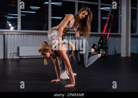 Weibliche Fitnesstrainerin führt persönliches Training durch. Junge attraktive Frau Liegestütze mit Schlaufen auf ihre Beine. Das Mädchen ist mit einem Trainer verlobt Stockfoto