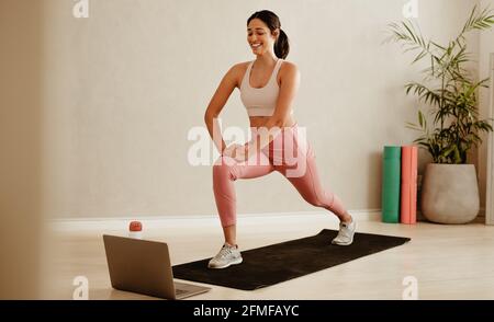 Weibliche Fitnesstrainerin führt Online-Trainingseinheiten per Videoanruf über einen Laptop durch. Frau in Sportbekleidung lehrt Ausfallschritt Übungen online mit Laptop. Stockfoto